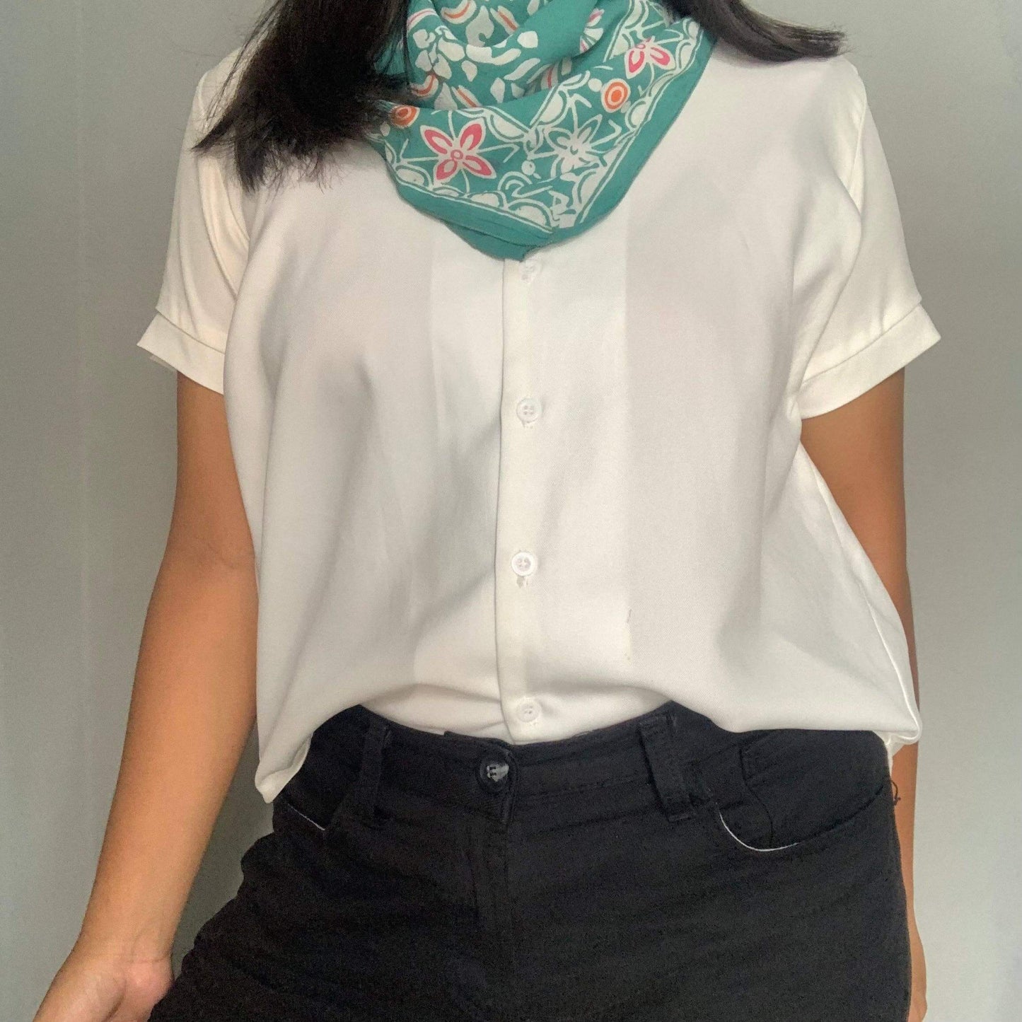 Person wearing a white blouse and dark pants with a floral headscarf on a plain background
