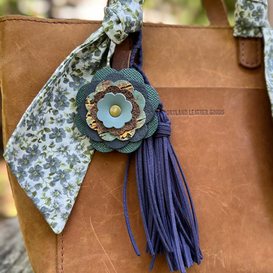 Brown leather bag with a decorative flower and tassel on a blurred natural background