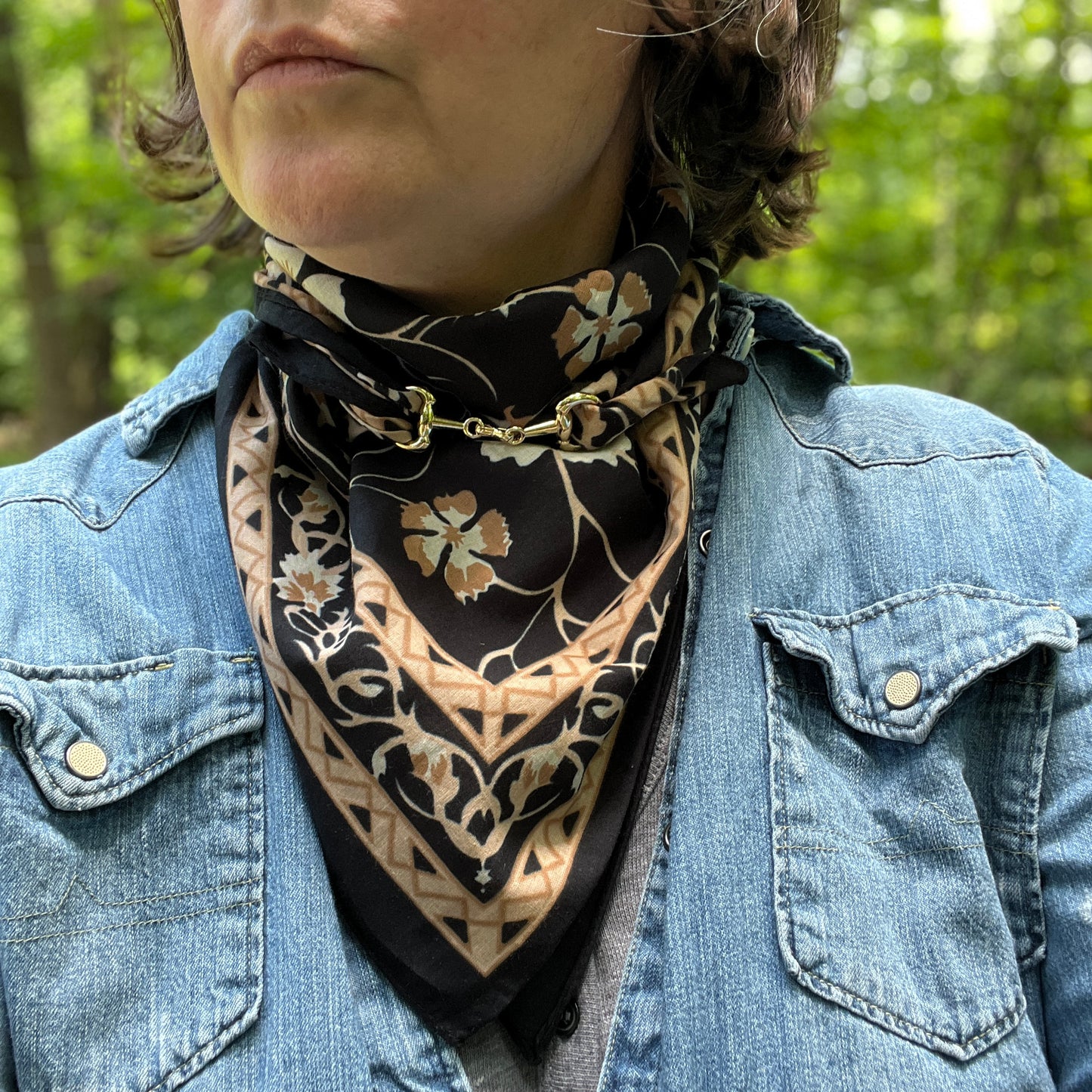 A close-up of a person outdoors wearing a black and beige floral bandana scarf tied around their neck, paired with a blue denim jacket.