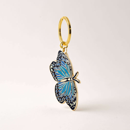 Gold butterfly keychain with blue wings on a light beige background