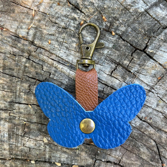 Blue butterfly-shaped keychain with a brown strap on a wooden surface