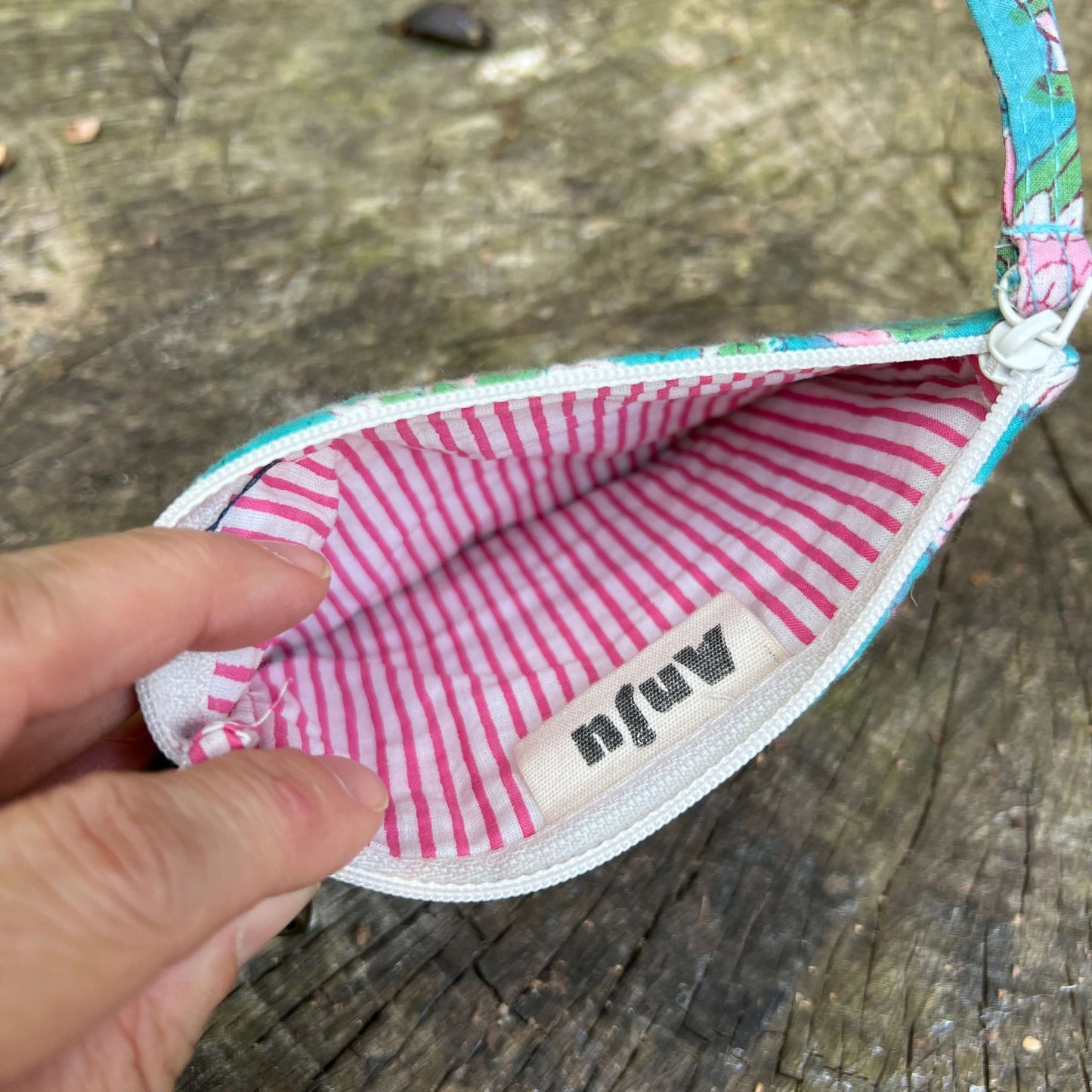 Small fabric pouch with pink and white striped interior on a wooden surface