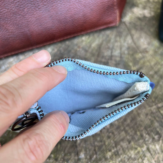 Hand opening a blue zippered pouch on a textured surface