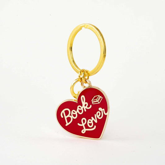 A gold-tone metal keychain featuring a red enamel heart charm with the words 'Book Lover' in white script and a small book icon, shown on a clean white background.