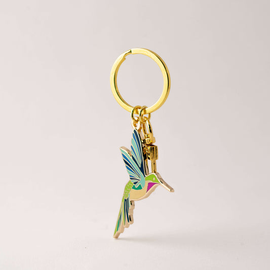 Gold keychain with a colorful hummingbird charm on a light gray background