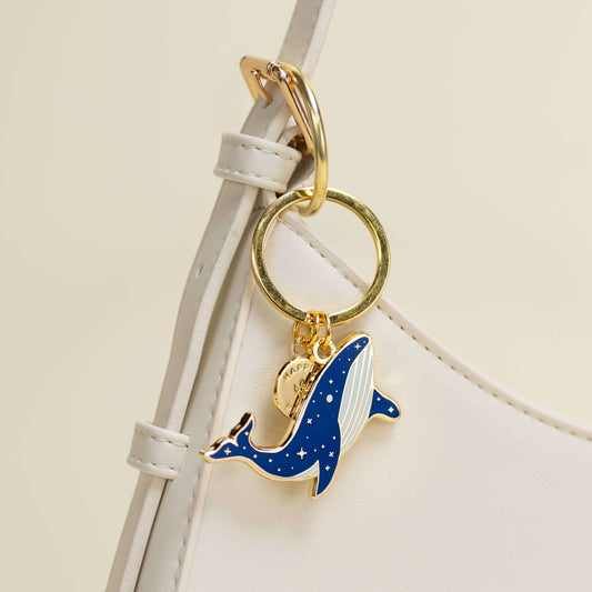 Keychain with a blue whale charm on a white strap against a beige background