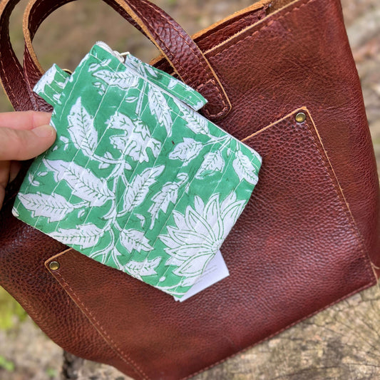 Green and white patterned zipper pouch held over a brown leather bag.