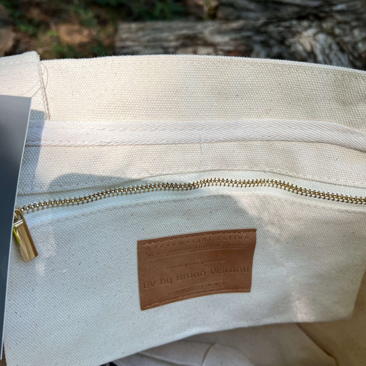 Close-up of a canvas tote bag interior showing a brass zipper, a tan leather brand patch