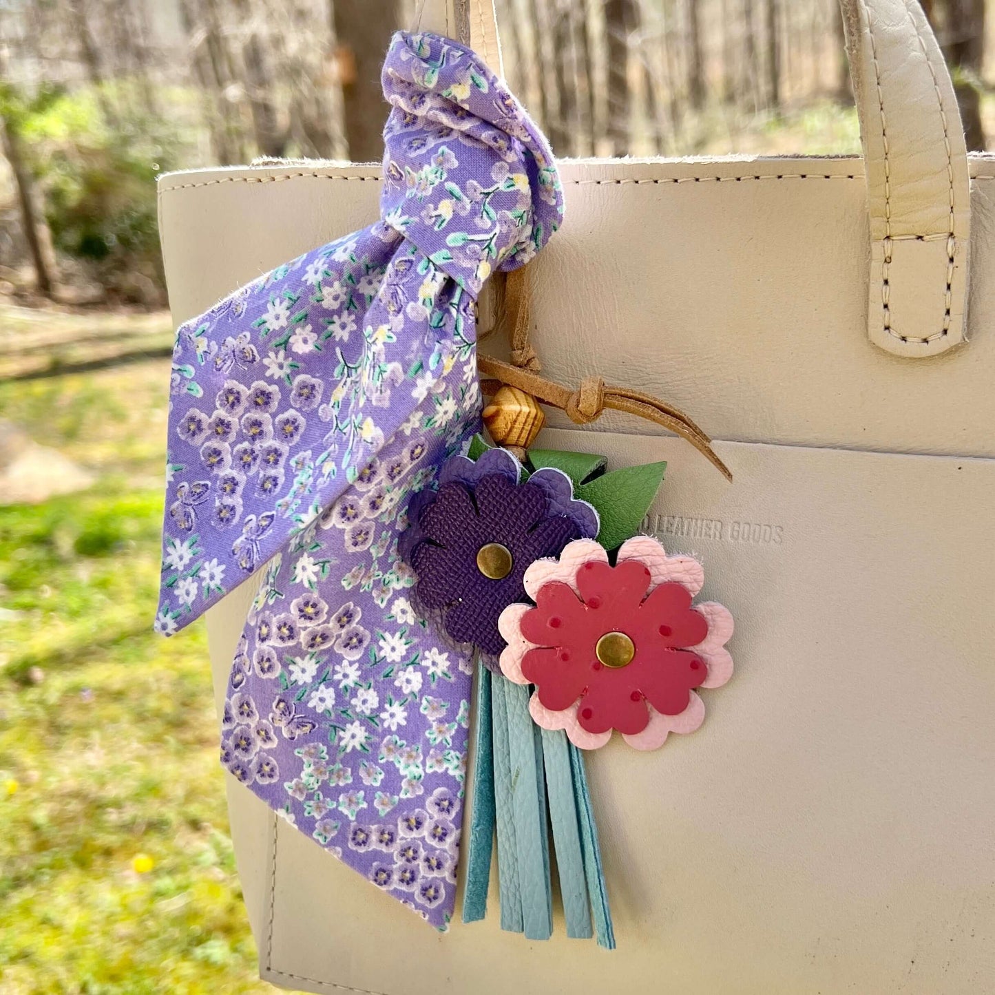 Beige handbag with a floral ribbon and decorative flowers attached outdoors.
