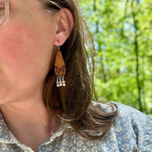 Close-up of a person wearing a leather earring with a butterfly design, outdoors.