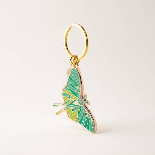 Green butterfly keychain with gold ring on a light beige background
