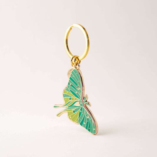 Green butterfly keychain with gold ring on a light beige background