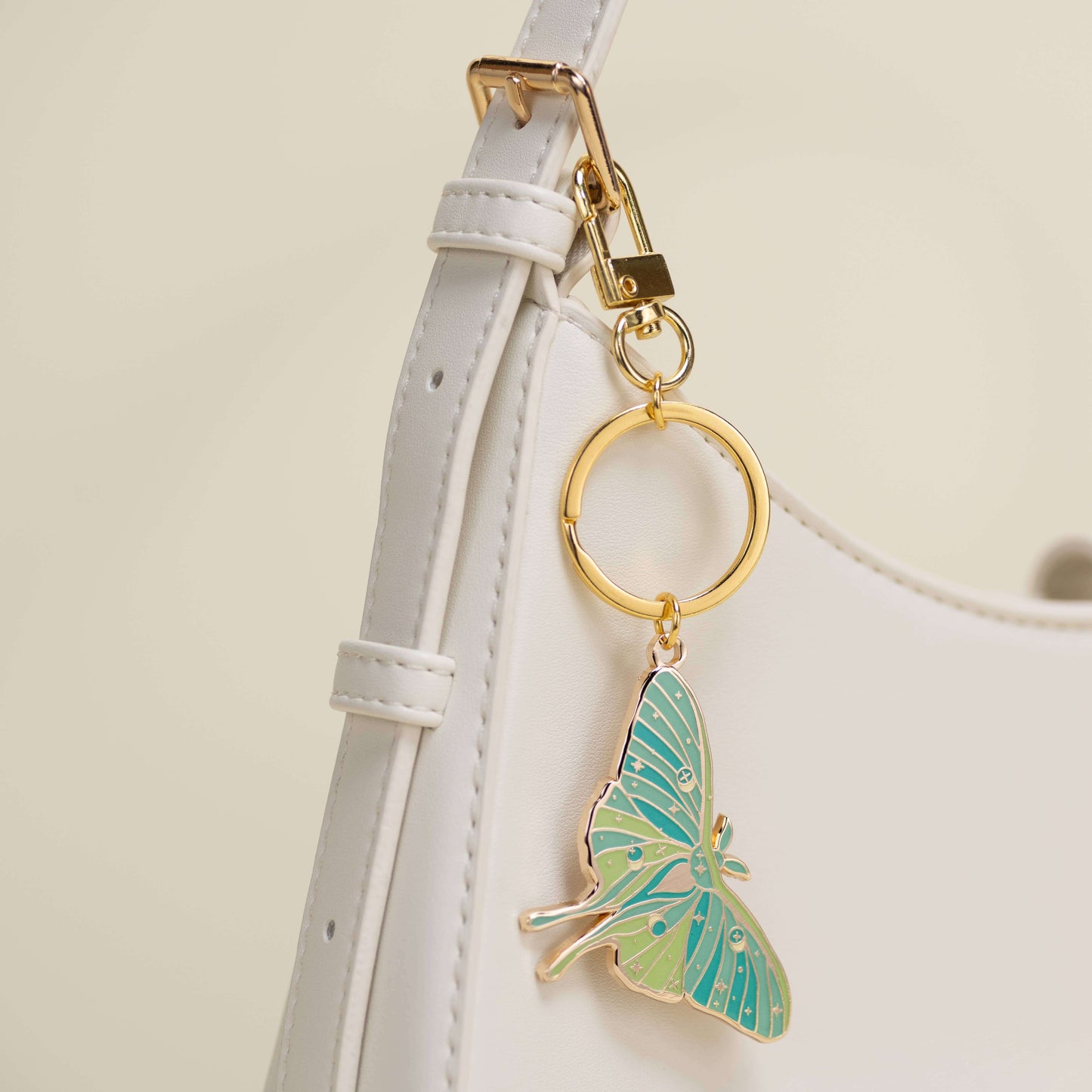 Butterfly keychain attached to a white strap with a gold ring on a light beige background