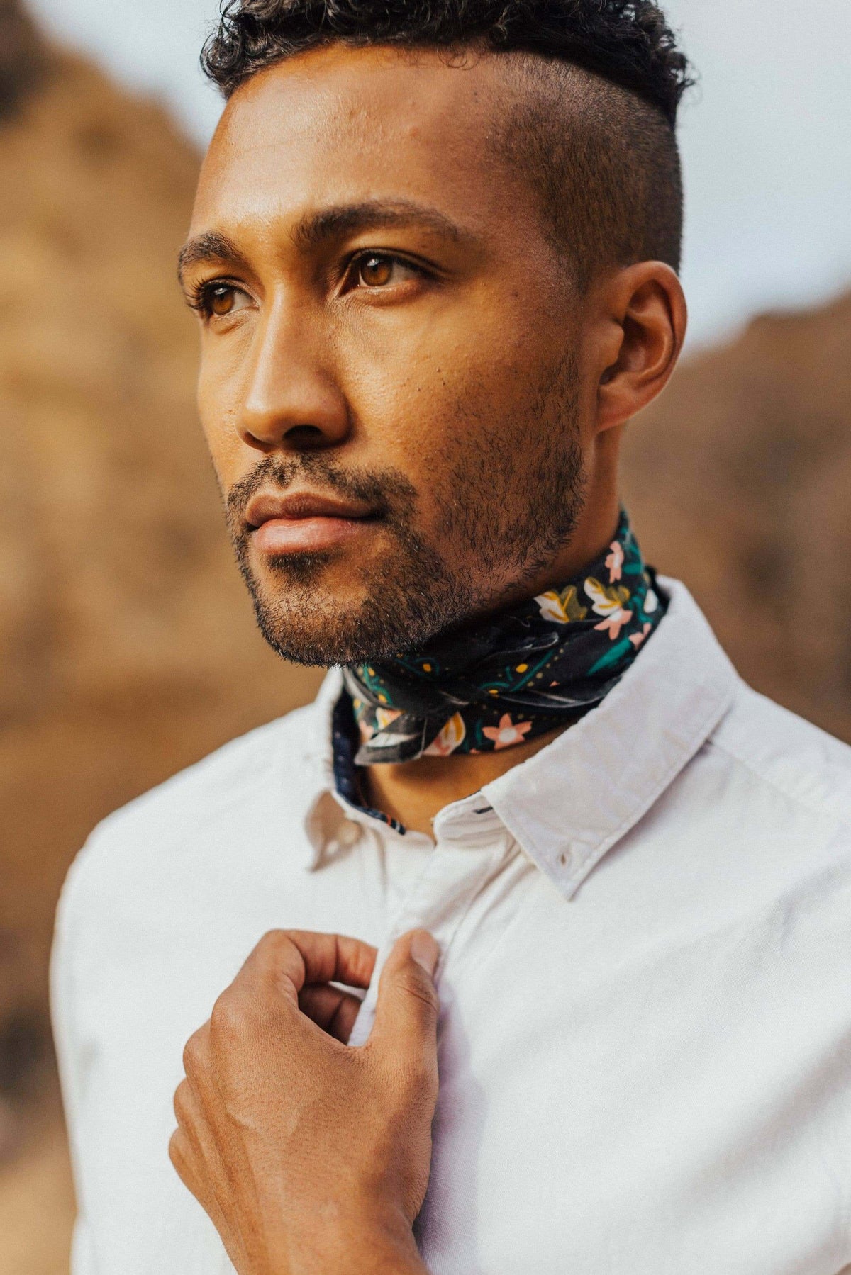 Man wearing a white shirt and floral neck scarf with a blurred natural background