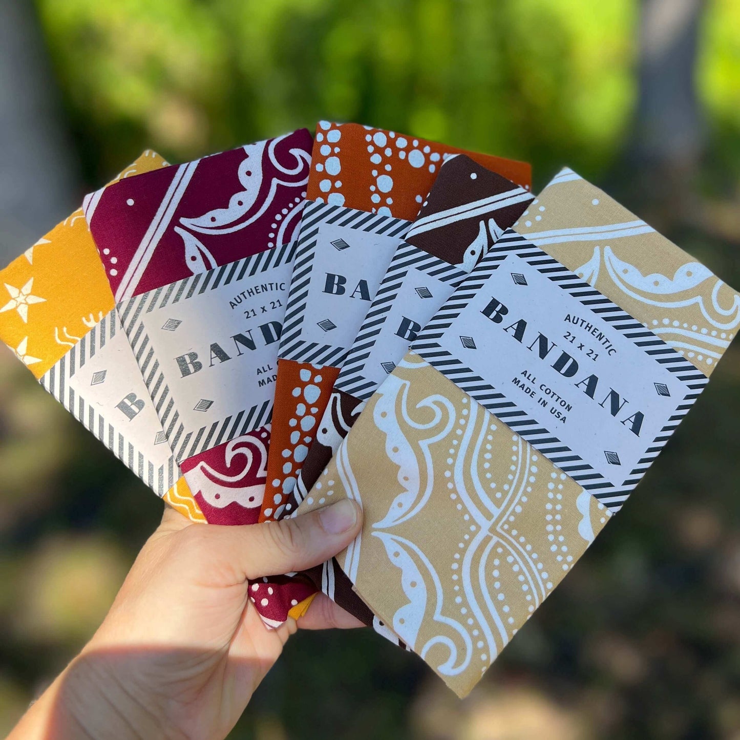 Hand holding a set of patterned bandanas with visible branding.