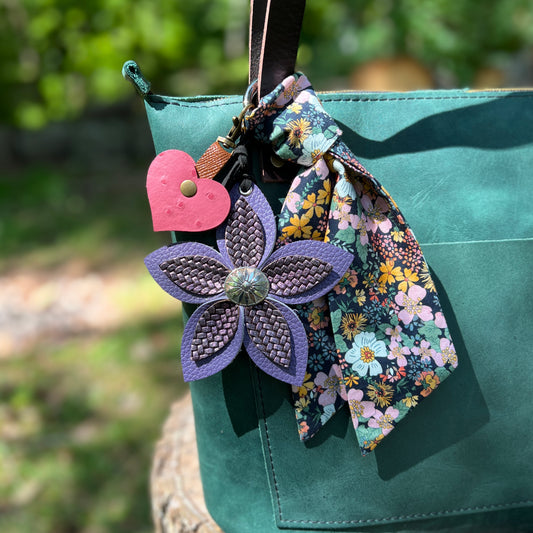 Decorative keychain with a purple flower and pink heart on a green bag with a floral ribbon.