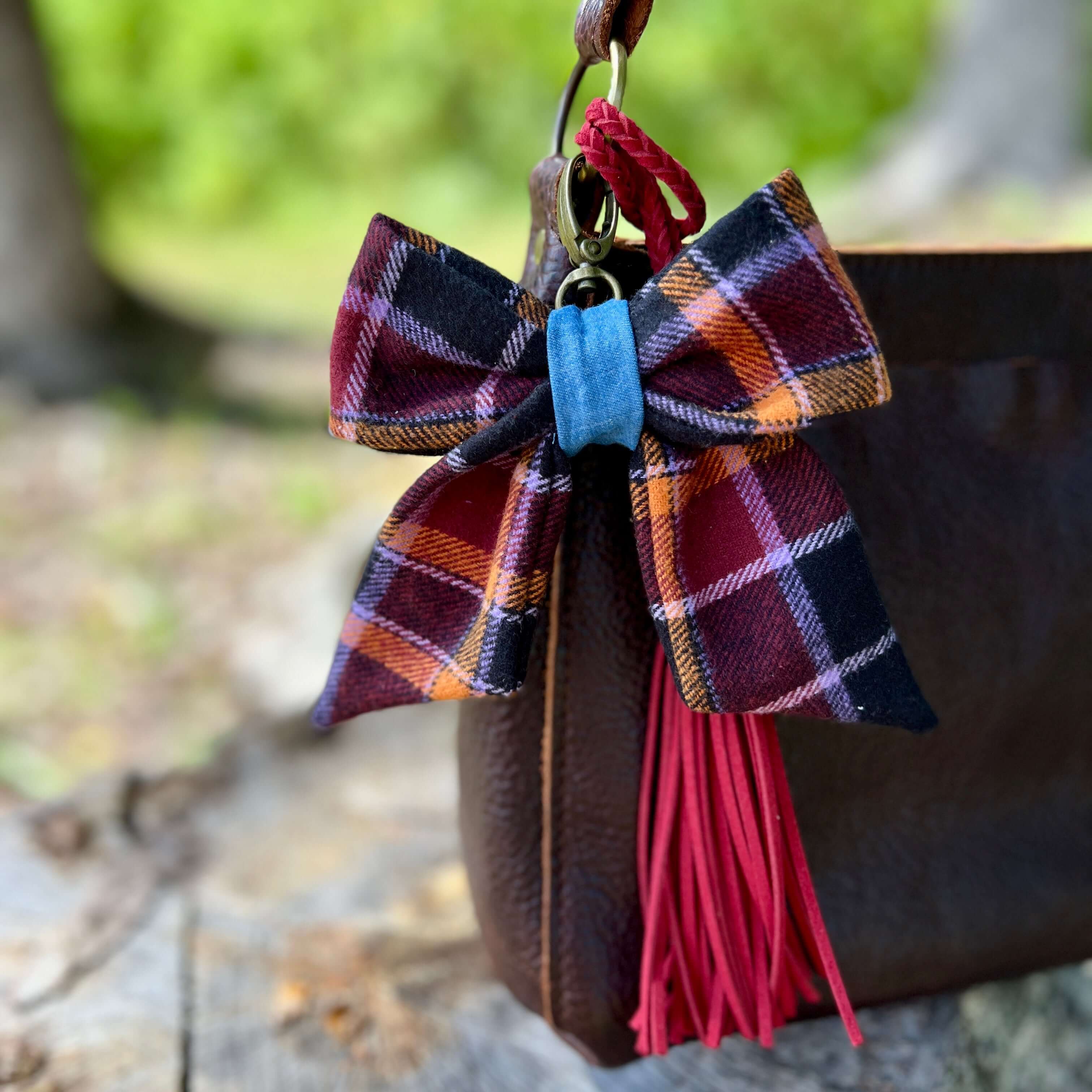 Plaid bow keychain with red tassel attached to a bag outdoors