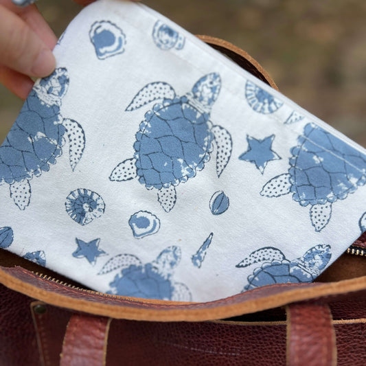 Fabric with blue turtle pattern held over a brown leather bag