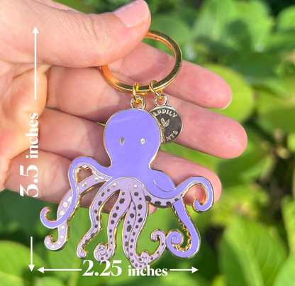 Purple octopus keychain held in a hand with measurements indicated, against a green leafy background.