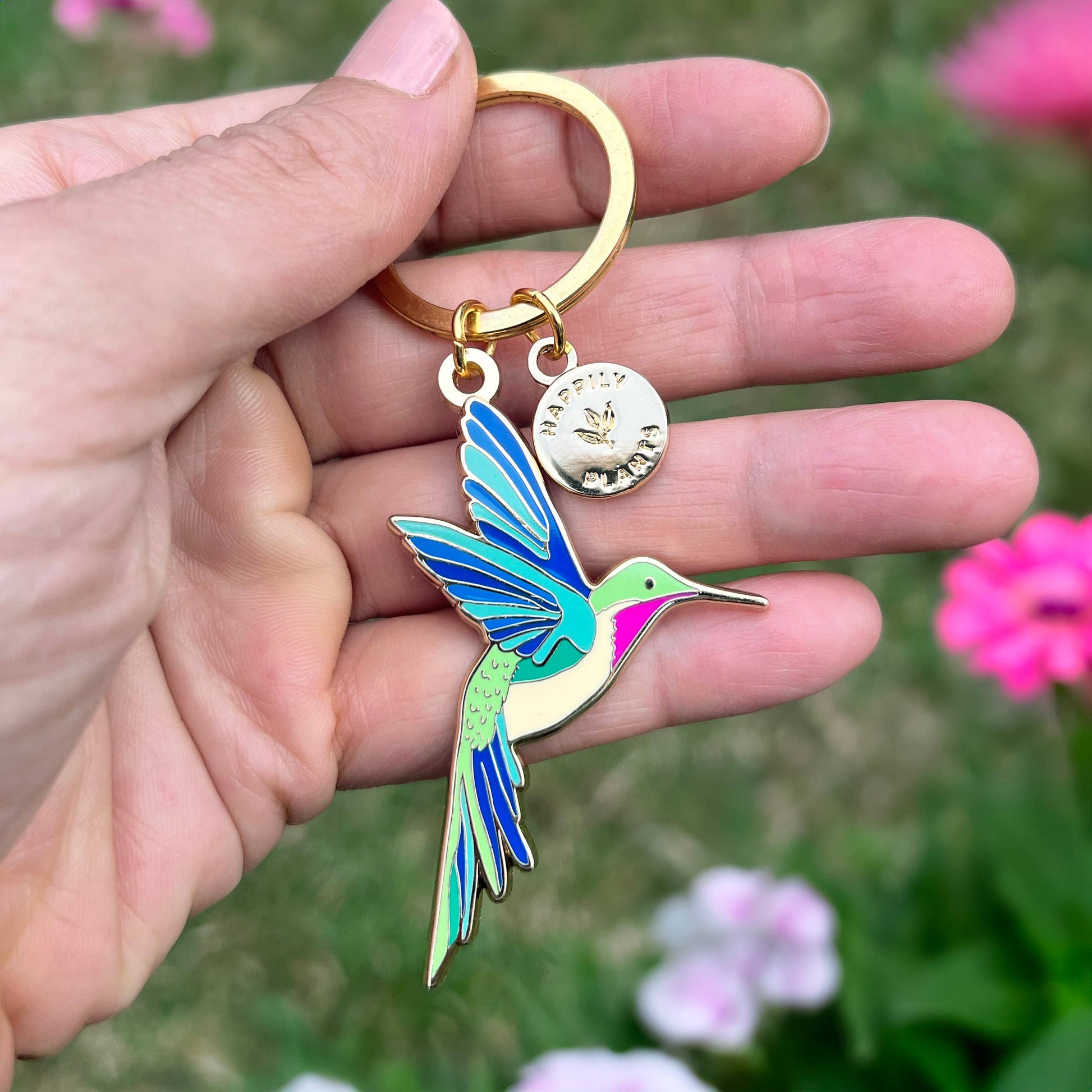 Hand holding a colorful hummingbird keychain with a blurred floral background