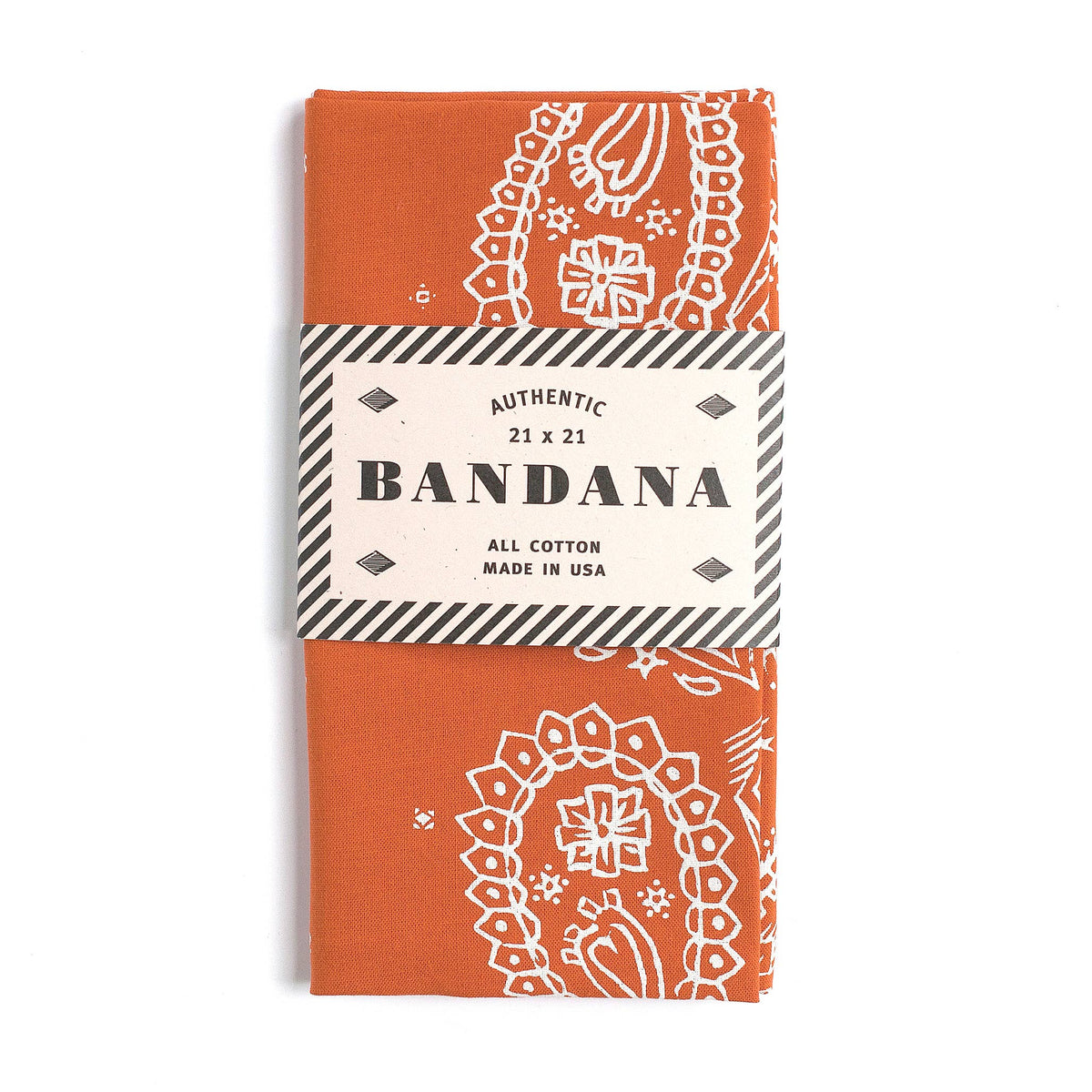 An orange cotton bandana with a white paisley pattern, wrapped in a paper band that reads 'AUTHENTIC 21 x 21 BANDANA ALL COTTON MADE IN USA'.