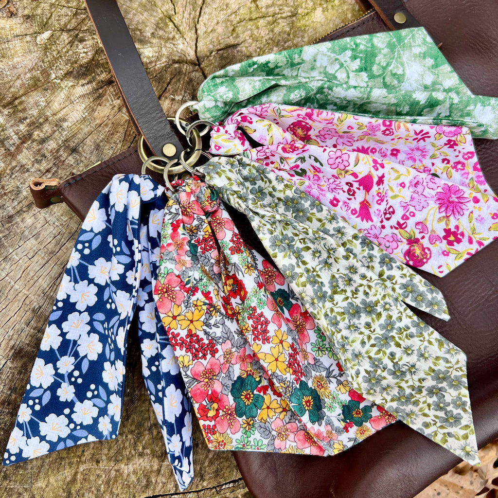 Floral fabric keychain hanging from a brown leather bag on a wooden surface