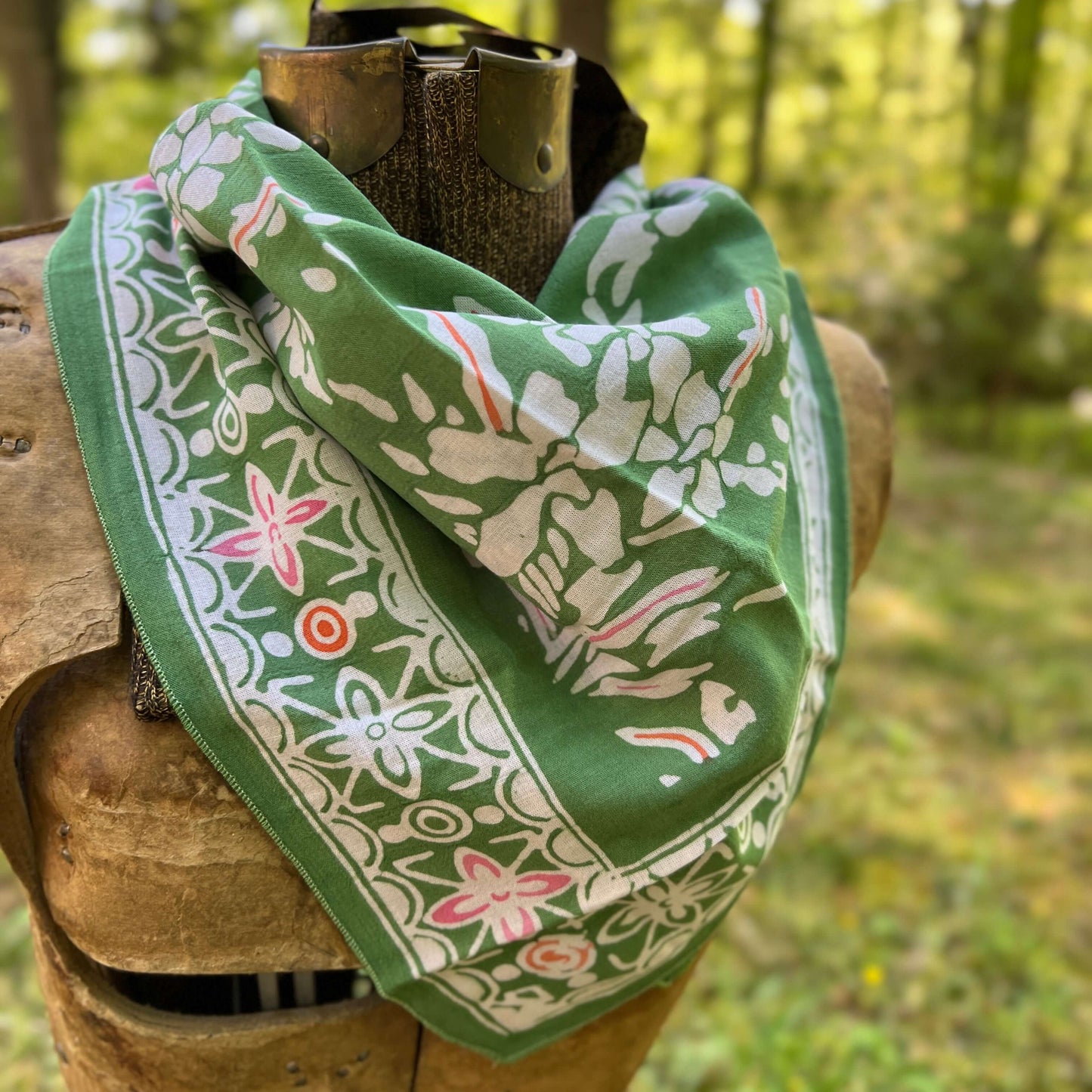 Green bandana with floral patterns draped over a wooden object in a natural setting.
