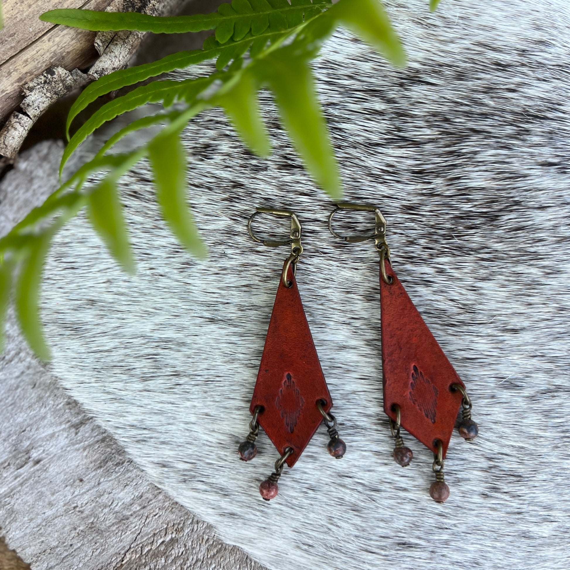 Western Style Leather Chandelier Earrings with Leopard JasperGenuine leather elongated diamond chandelier earrings. Stamped with a southwestern motif, dyed saddle tan and accented with leopard jasper dangles. Earrings dangle just under 3" long total Gold