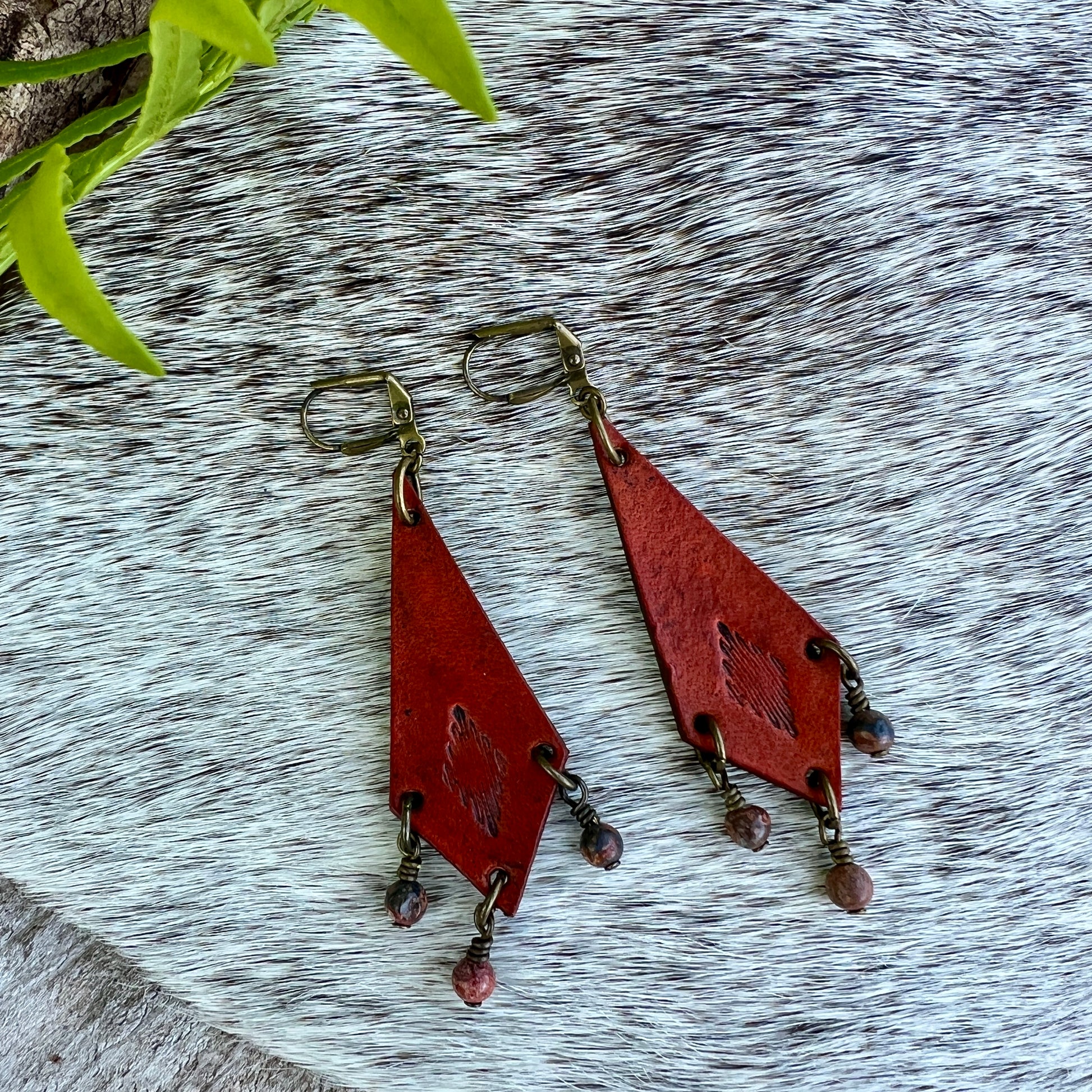 Western Style Leather Chandelier Earrings with Leopard JasperGenuine leather elongated diamond chandelier earrings. Stamped with a southwestern motif, dyed saddle tan and accented with leopard jasper dangles. Earrings dangle just under 3" long total Gold