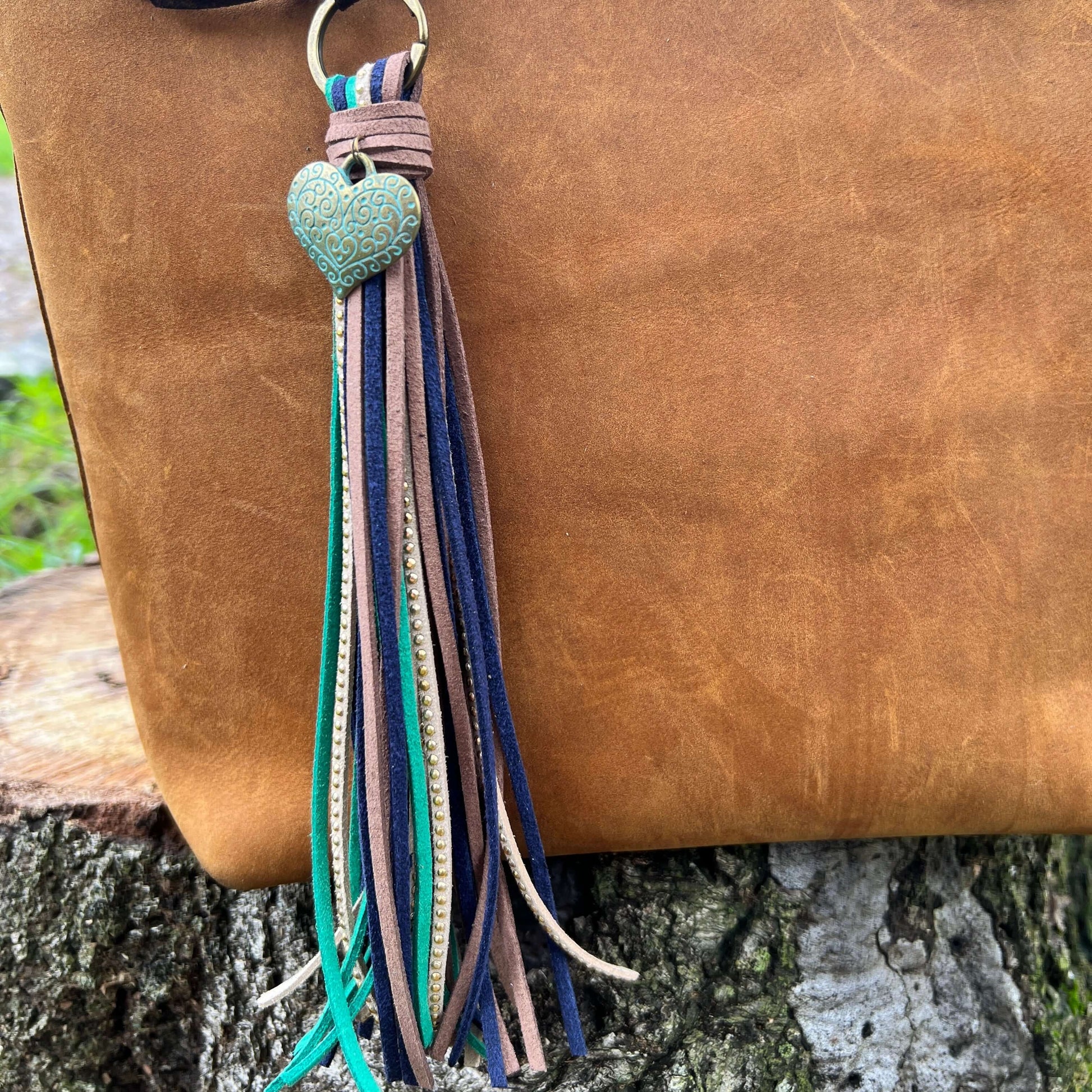 Tassel Purse Charm with Heart CharmChic and simple faux suede tassel purse charm with give your tote or bag an instant boho vibe. Crafted with faux suede in navy, sea green, warm brown and tan with golden studs and accented with heart charm. Long loop wor