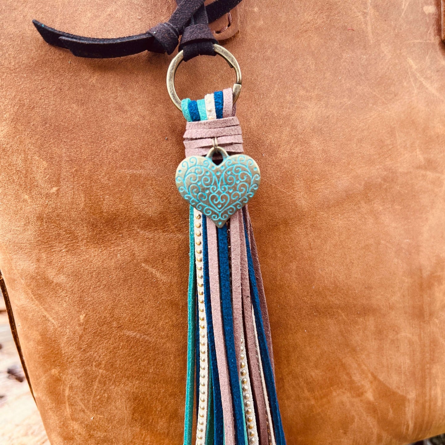 Tassel Purse Charm with Heart CharmChic and simple faux suede tassel purse charm with give your tote or bag an instant boho vibe. Crafted with faux suede in navy, sea green, warm brown and tan with golden studs and accented with heart charm. Long loop wor