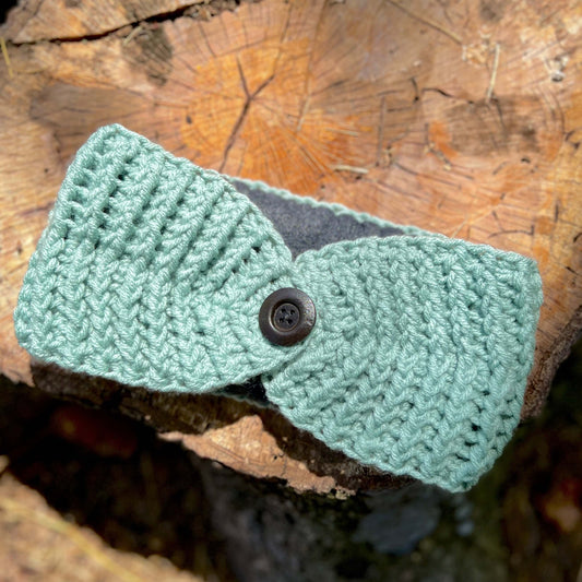 Winter Headband with Fleece Lining - Light Sage GreenKeep your ears nice and warm without messing up your do. Crocheted with super soft acrylic yarn and lined with fleece for extra warmth. Button can be worn in the back, front or on the side. 4.75" wide -