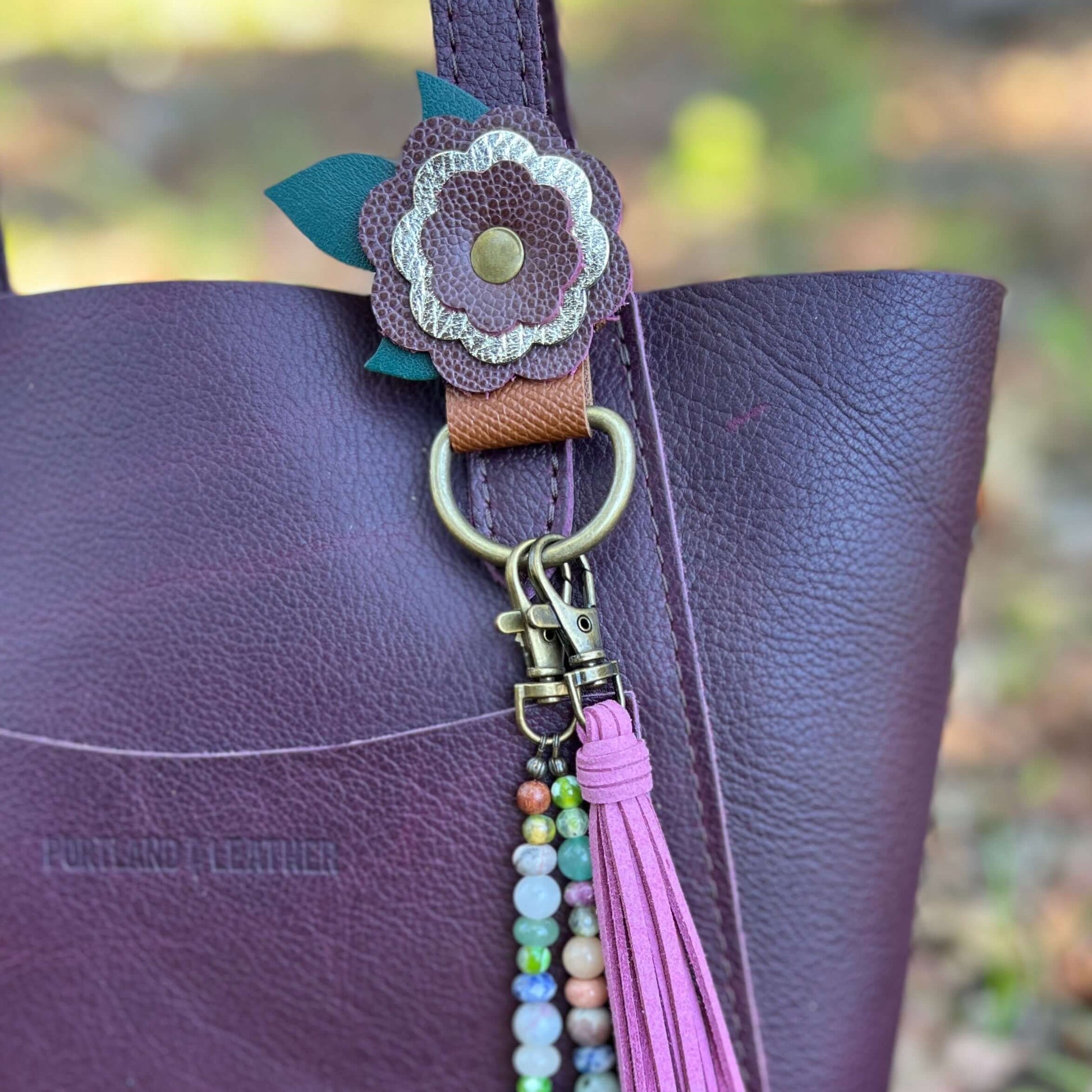 Purse Charm Holder - FlowersNew! keep your bag and purse charms in place with a handy snap on holder. Crafted with sturdy leather and accented with a layered flower, these charm holders will be the best thing you bought all year. Snaps at 2.75" and fits m