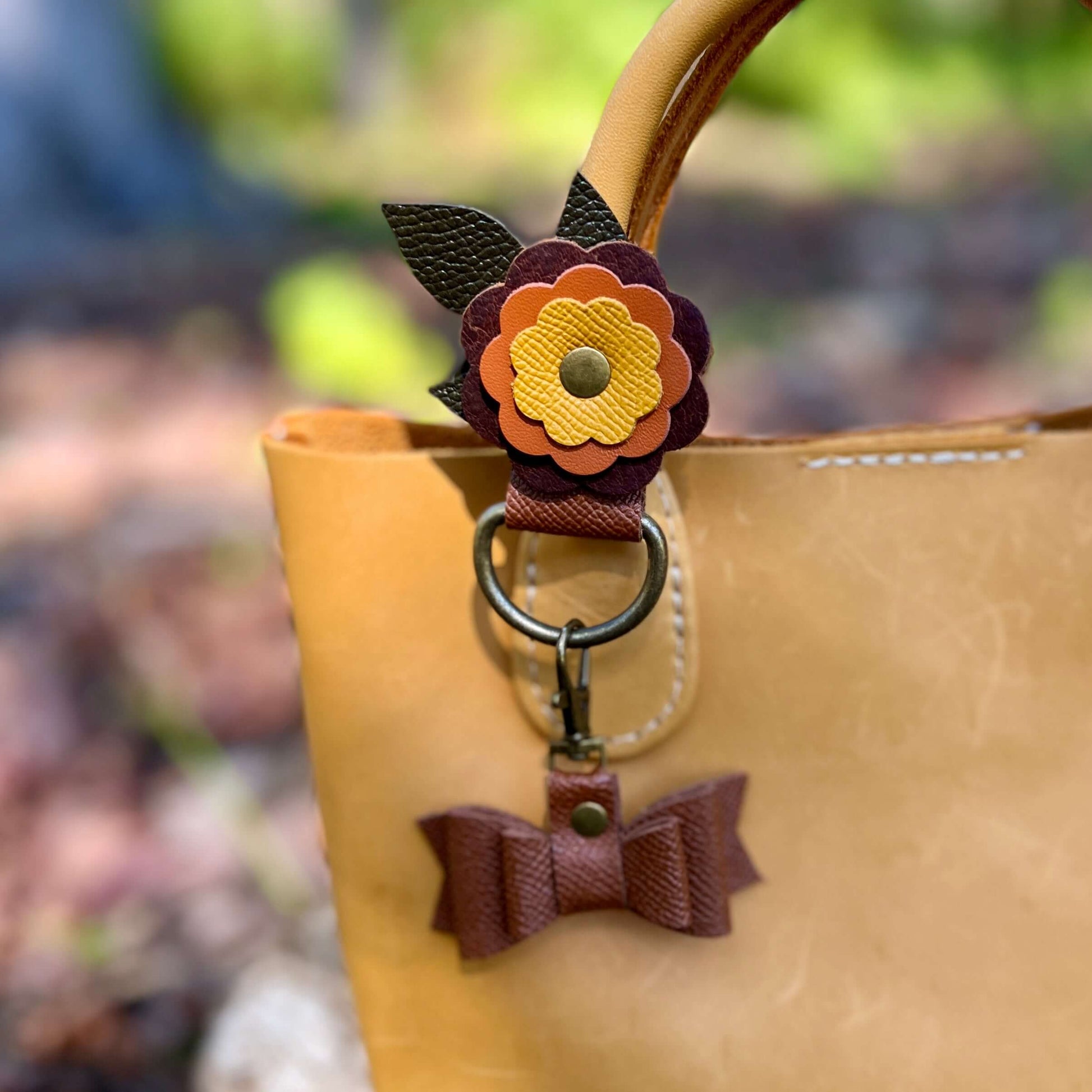 Purse Charm Holder - FlowersNew! keep your bag and purse charms in place with a handy snap on holder. Crafted with sturdy leather and accented with a layered flower, these charm holders will be the best thing you bought all year. Snaps at 2.75" and fits m