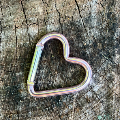 Lavender  heart-shaped carabiner, resting on a textured, weathered tree stump.