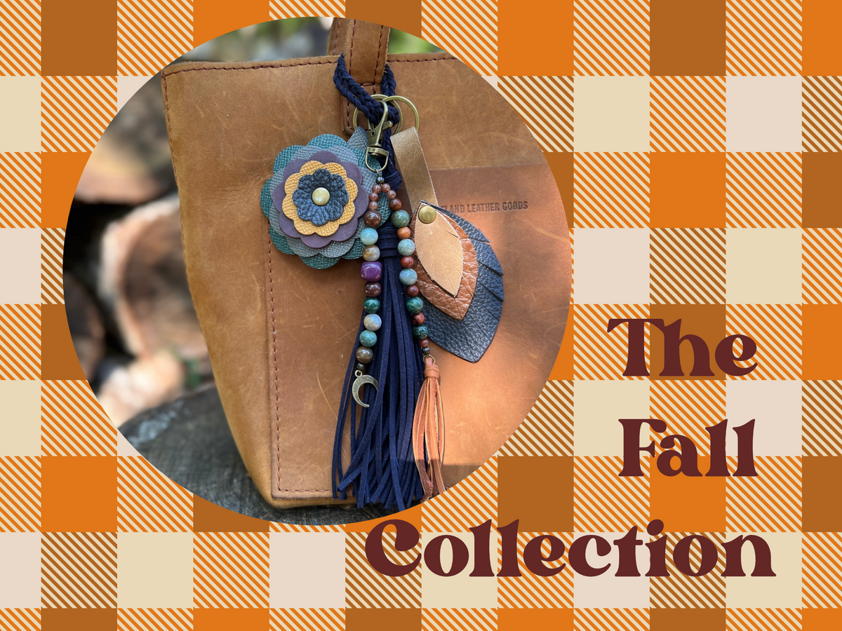 leather flower and leaf bag charms with beaded tassel and navy blue tassel bag charm on brown tote bag. Words The Fall Collection on plaid background
