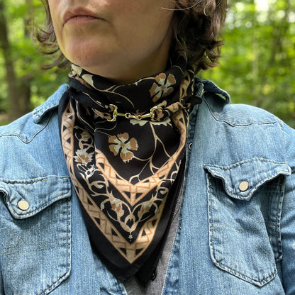 A close-up of a person outdoors wearing a black and beige floral bandana scarf tied around their neck, paired with a blue denim jacket.