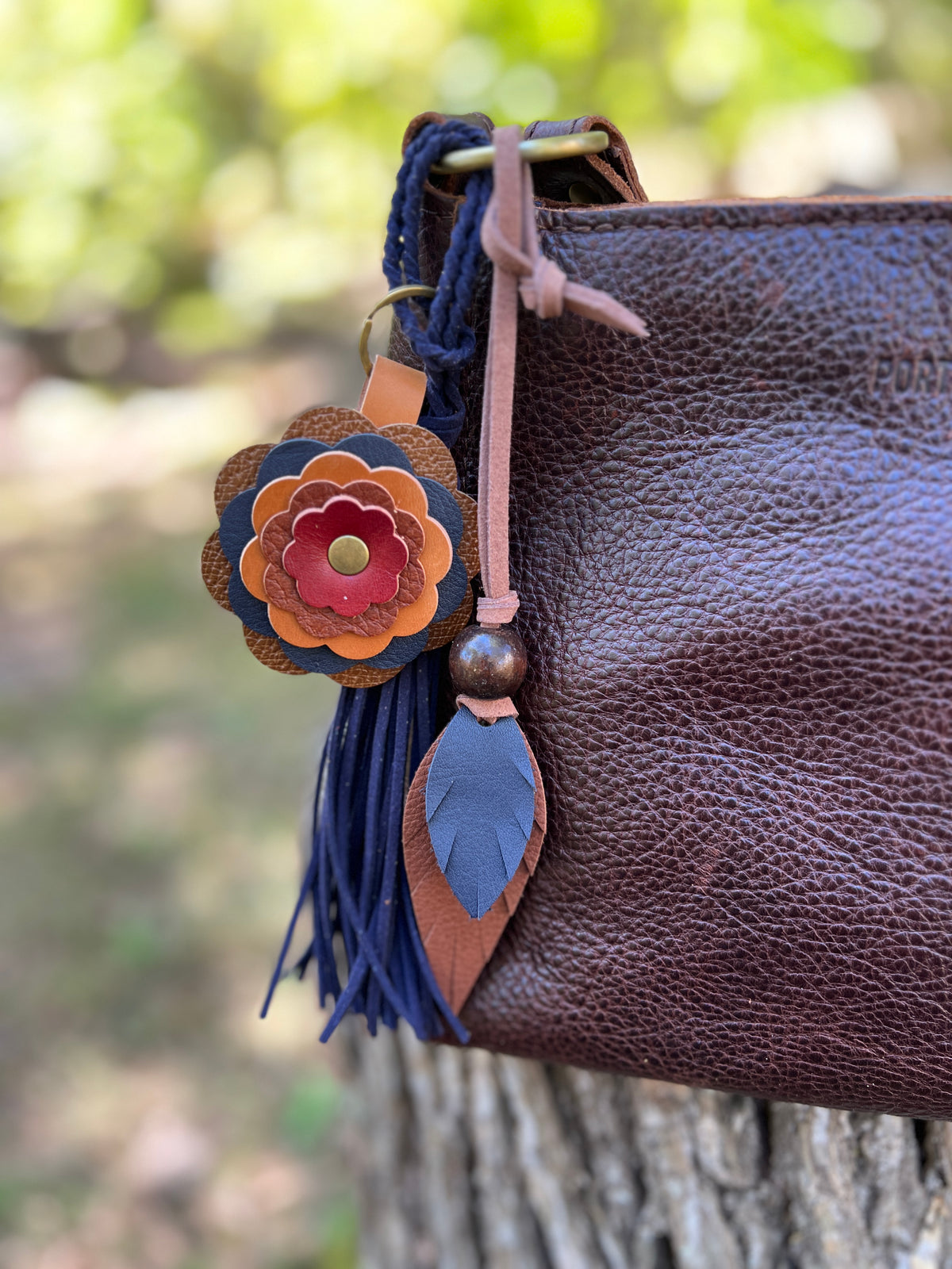 blue and brown leather feather bag charm with flower and navy tassel on brown bag
