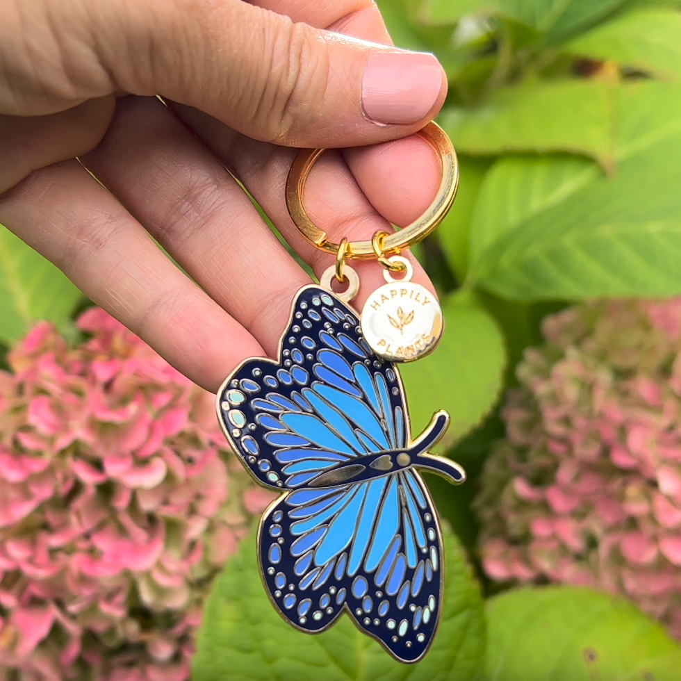 Hand holding a blue butterfly keychain with a blurred floral background
