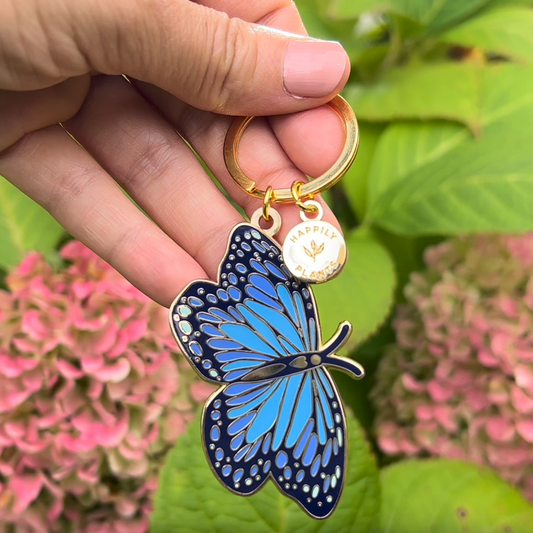 Hand holding a blue butterfly keychain with a blurred floral background