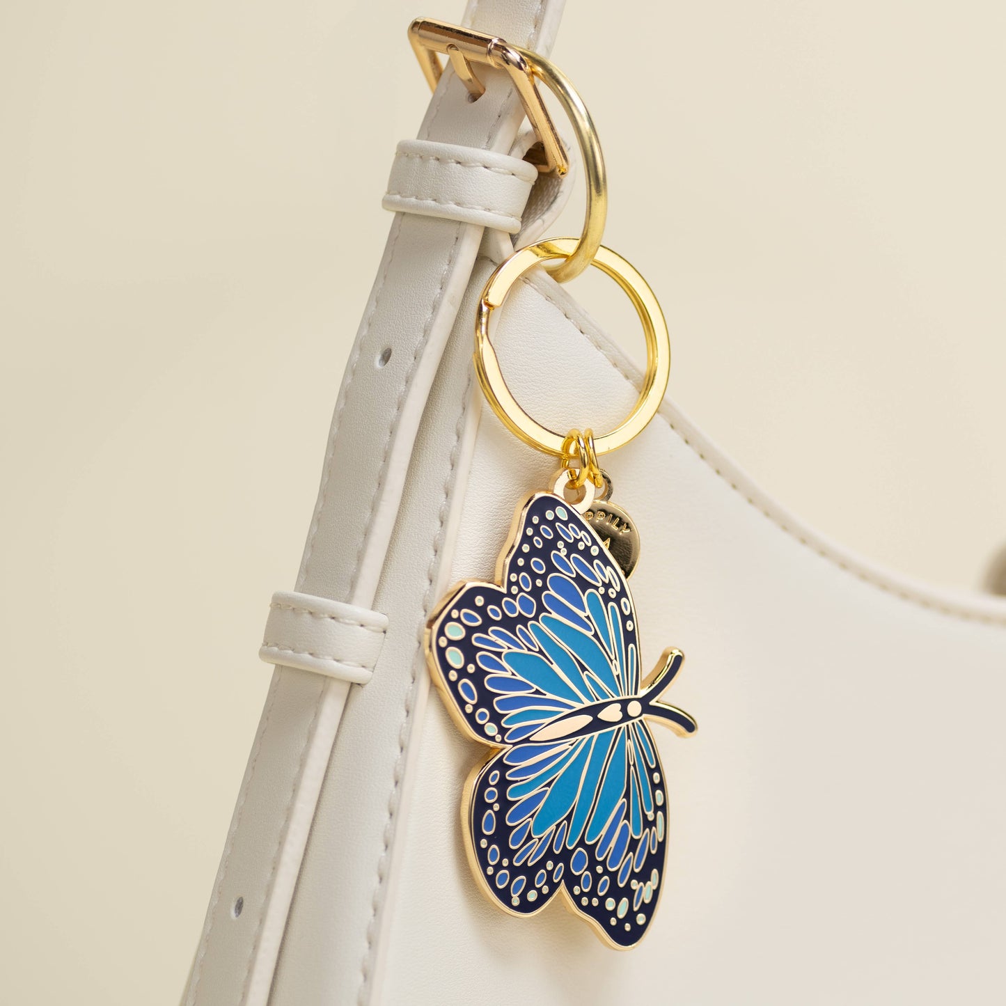 Blue butterfly keychain attached to a white strap with gold rings on a beige background