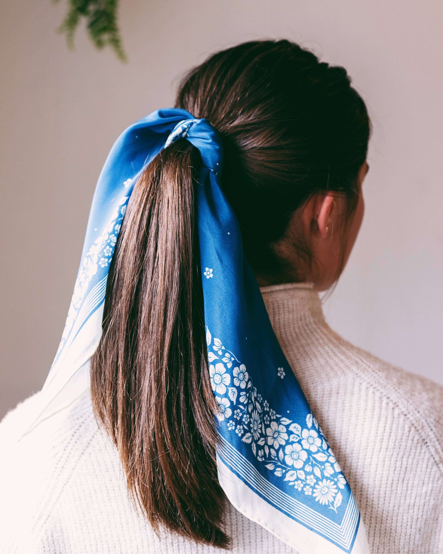 Person with a blue floral headscarf tied in a ponytail against a neutral background