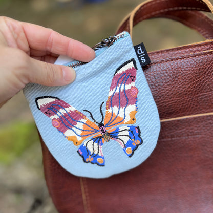 Small pouch with a butterfly design held by a hand against a brown leather bag.
