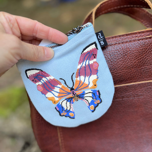 Small pouch with a butterfly design held by a hand against a brown leather bag.