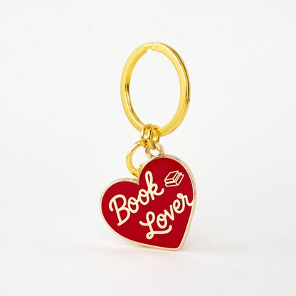 A gold-tone metal keychain featuring a red enamel heart charm with the words 'Book Lover' in white script and a small book icon, shown on a clean white background.