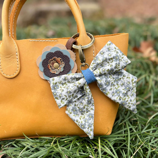 Floral bow keychain attached to a yellow handbag on grass