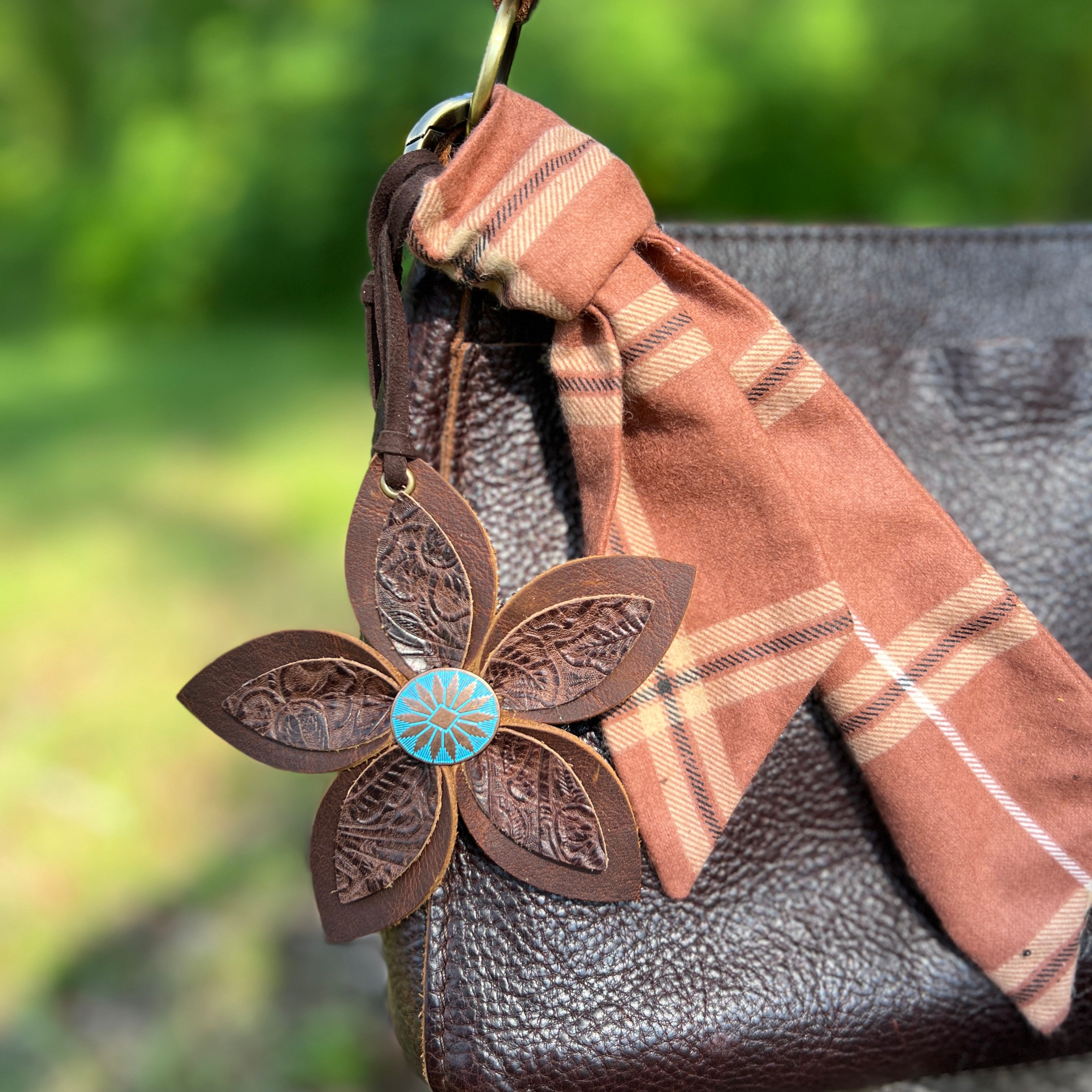 Leather flower keychain attached to a plaid bag with a blurred green background