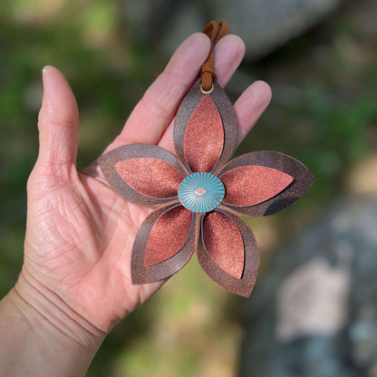 Hand holding a decorative leather flower bag charm with a blurred natural background