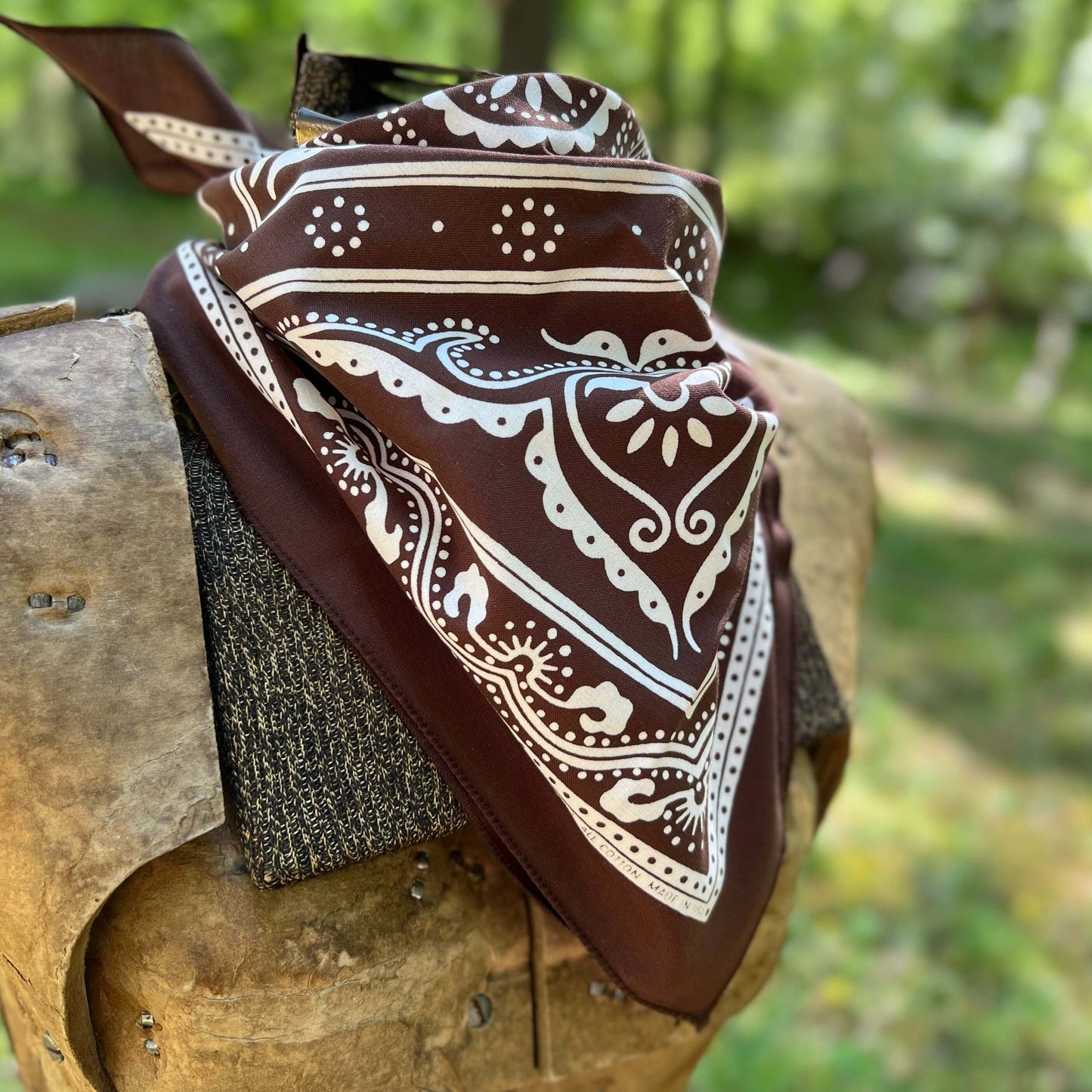 Brown bandana with white patterns draped over a wooden surface outdoors.