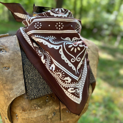 Brown bandana with white patterns draped over a wooden surface outdoors.